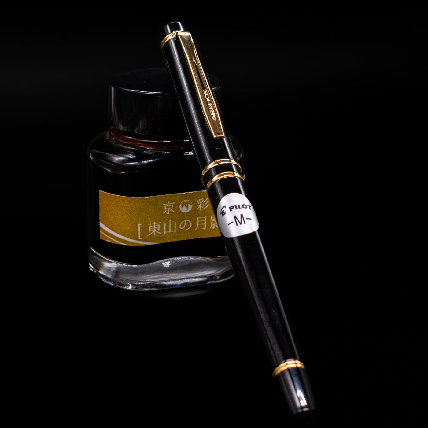 Pilot Grance Fountain Pen - Black capped, leaning against an ink bottle. 