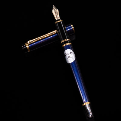 Pilot Grance Fountain Pen - Navy Blue laying on top of its cap in a crossed position showing full view of the entire uncapped pen.