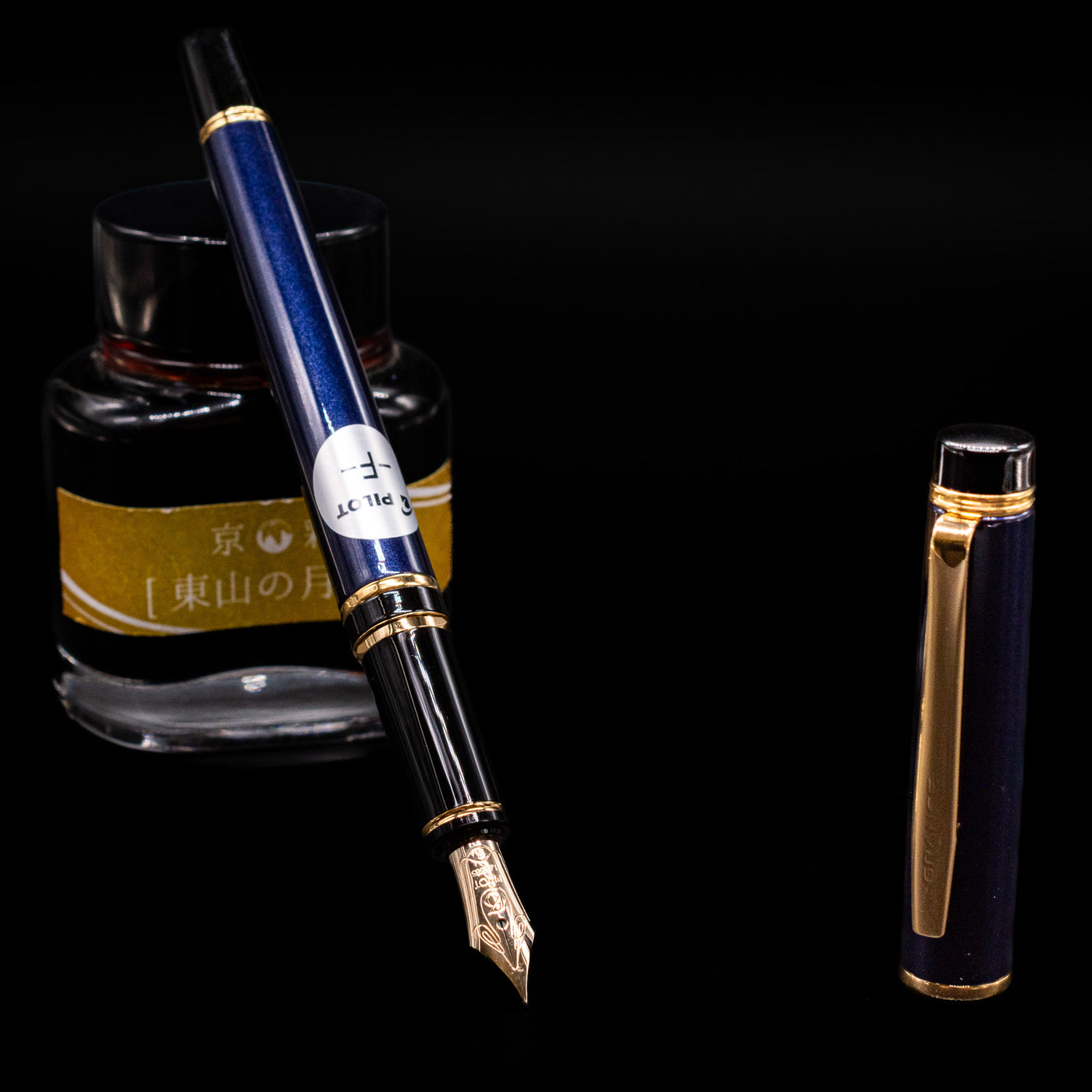 Pilot Grance Fountain Pen - Navy Blue leaning on an ink bottle uncapped showcasing the detailing on the nib.