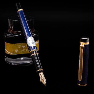 Pilot Grance Fountain Pen - Navy Blue leaning on an ink bottle uncapped showcasing the detailing on the nib.