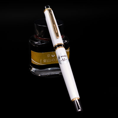 Pilot Grance Fountain Pen - Pearl White capped, leaning against an ink bottle. 