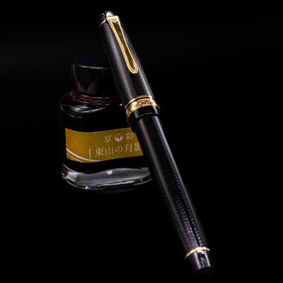 Preowned Pilot Justus 95 Net Black fountain pen shown capped, resting at an angle against an ink bottle. The black resin body features a subtle net-pattern finish with gold trim, reflecting a classic, refined look.