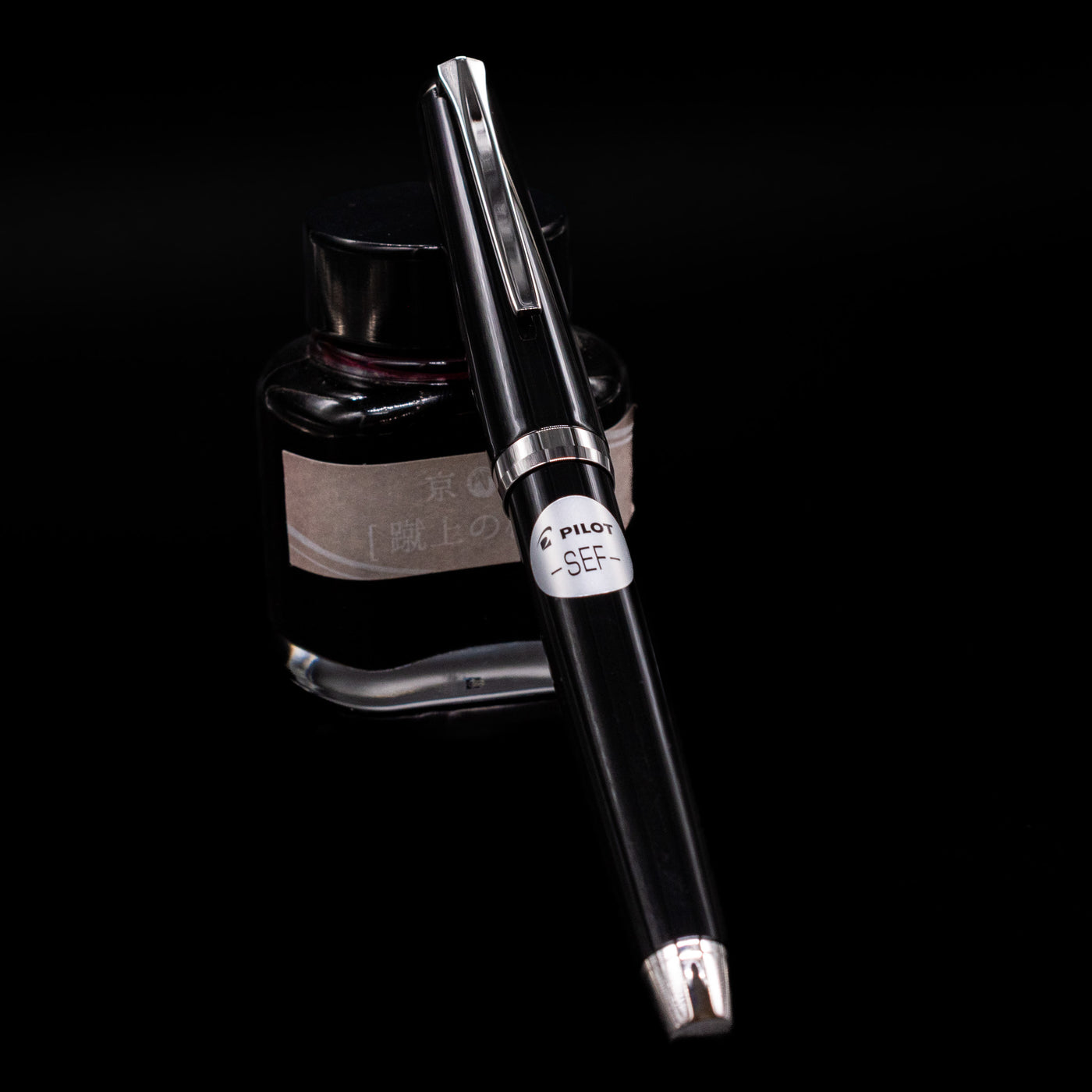 Pilot Metal Falcon Fountain Pen - Black capped, leaning against an ink bottle. 