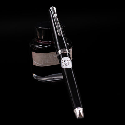 Pilot Metal Falcon Fountain Pen - Black capped, leaning against an ink bottle. 