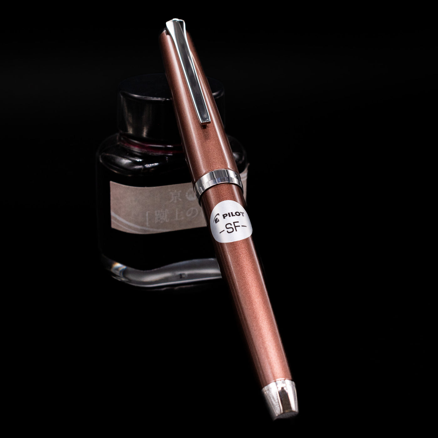 Pilot Metal Falcon Fountain Pen - Brown capped, leaning against an ink bottle. 