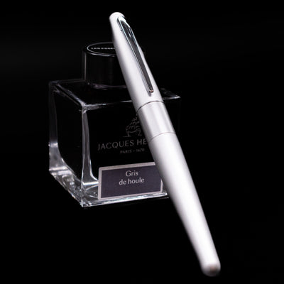 Pilot Metropolitan Fountain Pen - Plain Silver capped, leaning against an ink bottle. 