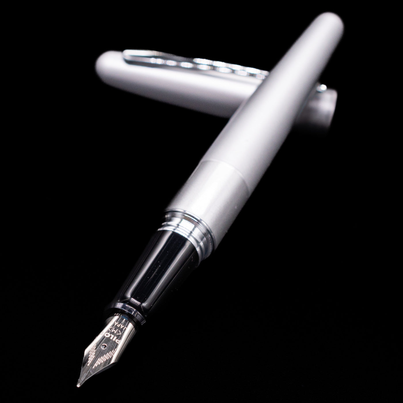 Pilot Metropolitan Fountain Pen - Plain Silver laying across its own cap, crossed, with a focus on the nib.