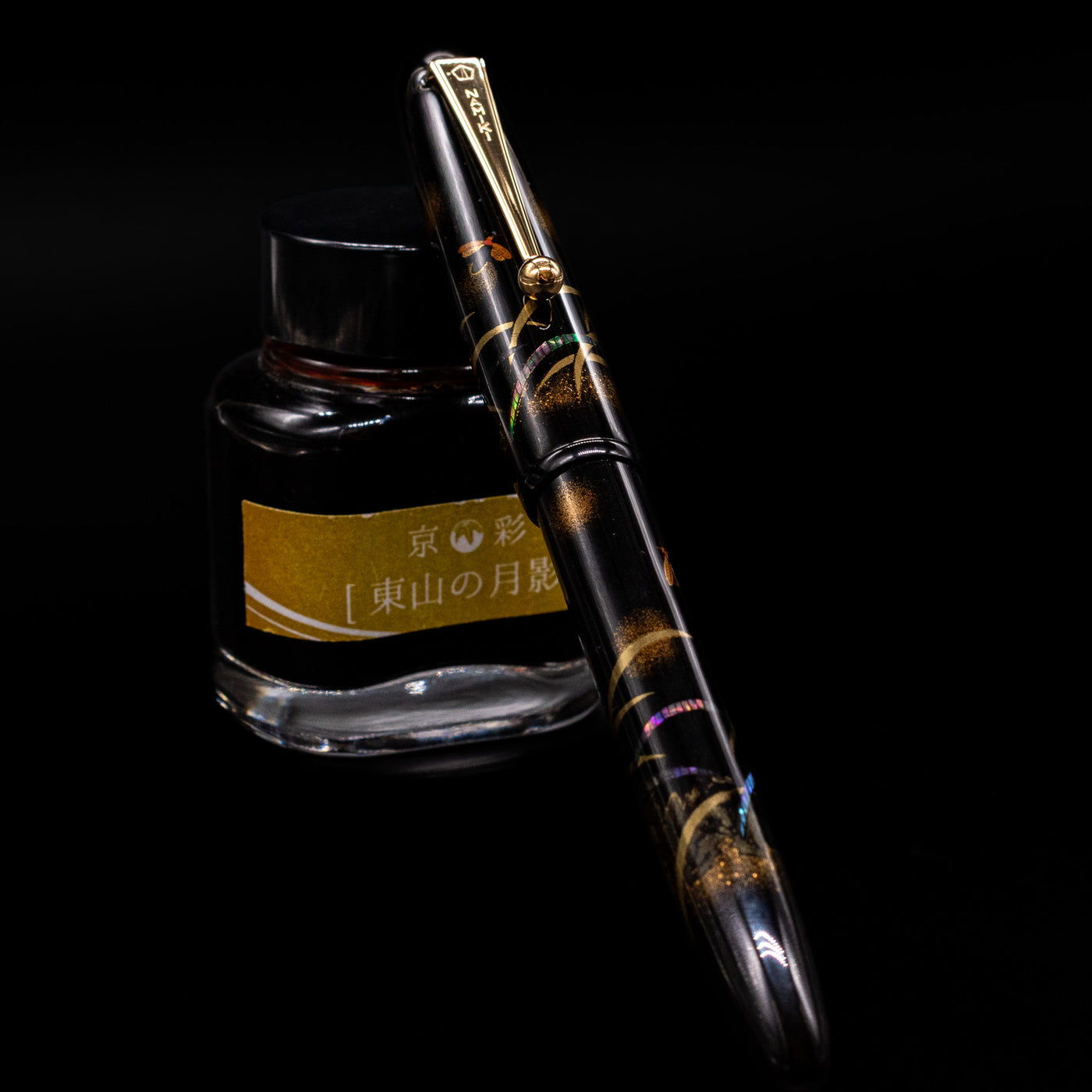 Pilot Namiki Yukari Maki-e Fountain Pen - Firefly capped, leaning against an ink bottle. 