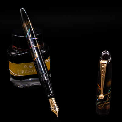 Pilot Namiki Yukari Maki-e Fountain Pen - Firefly leaning on an ink bottle uncapped showcasing the detailing on the nib.