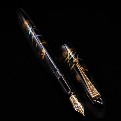 A full view of the Pilot Namiki Yukari Maki-e Fountain Pen - Firefly uncapped, with its cap laying next to the pen. 