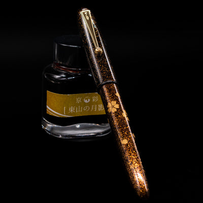 Pilot Namiki Yukari Maki-e Fountain Pen - Sakura Fubuki capped, leaning against an ink bottle. 