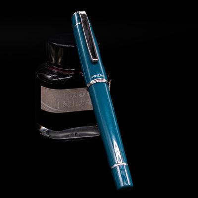 Pilot Prera Fountain Pen - Empress Teal capped, leaning against an ink bottle. 