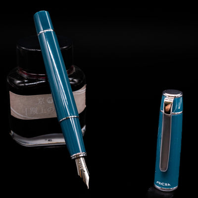 Pilot Prera Fountain Pen - Empress Teal leaning on an ink bottle uncapped showcasing the detailing on the nib.