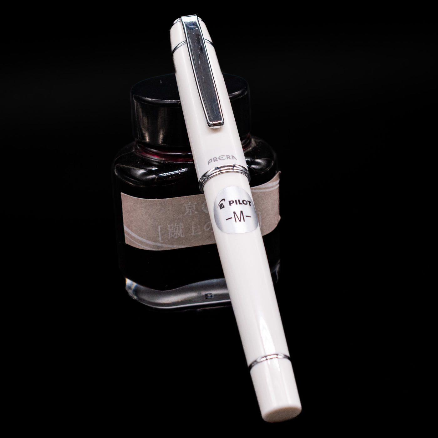 Pilot Prera Fountain Pen - Porcelain White capped, leaning against an ink bottle. 
