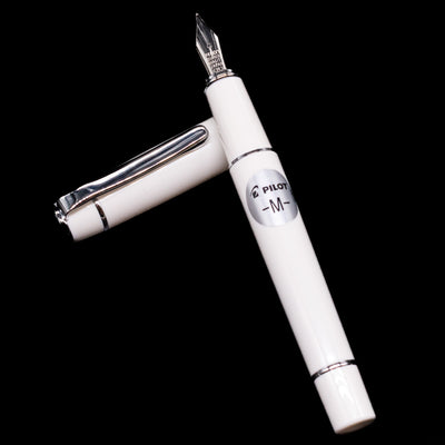 Pilot Prera Fountain Pen - Porcelain White laying on top of its cap in a crossed position showing full view of the entire uncapped pen.