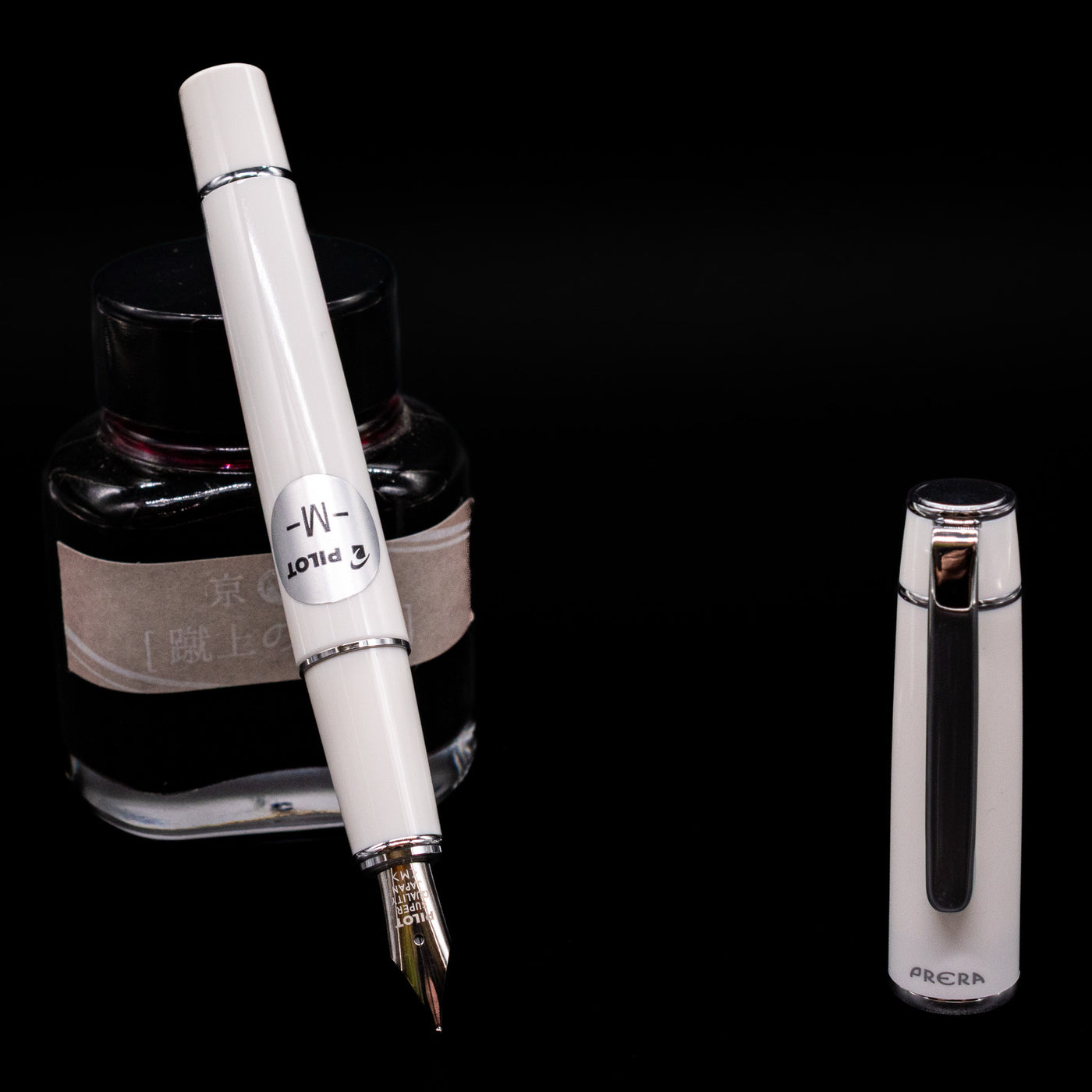 Pilot Prera Fountain Pen - Porcelain White leaning on an ink bottle uncapped showcasing the detailing on the nib.
