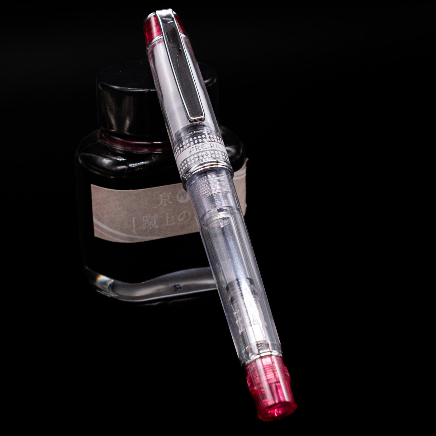 Pilot Prera Fountain Pen - Red capped, leaning against an ink bottle. 