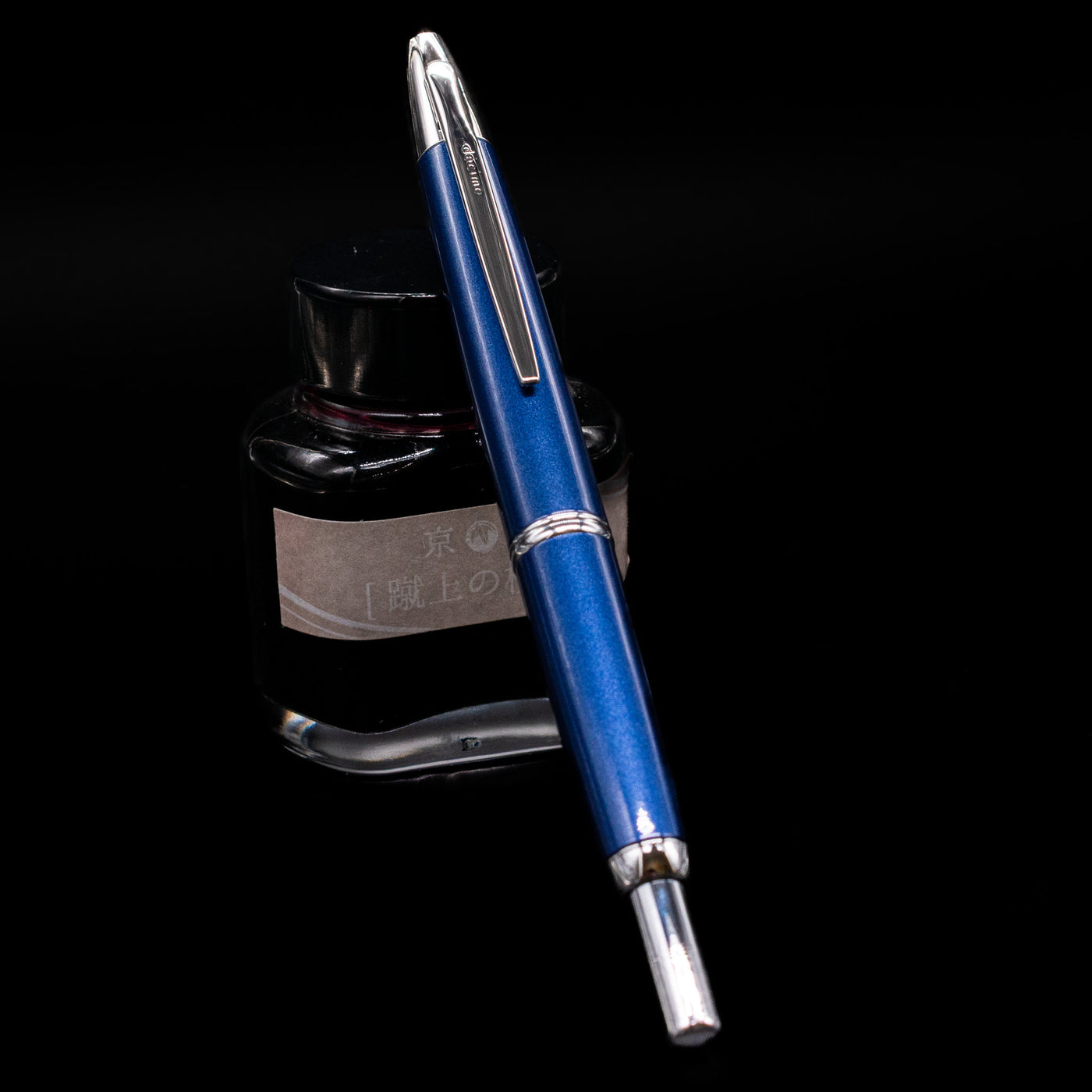 Pilot Vanishing Point Decimo Fountain Pen - Navy Blue capped, leaning against an ink bottle.