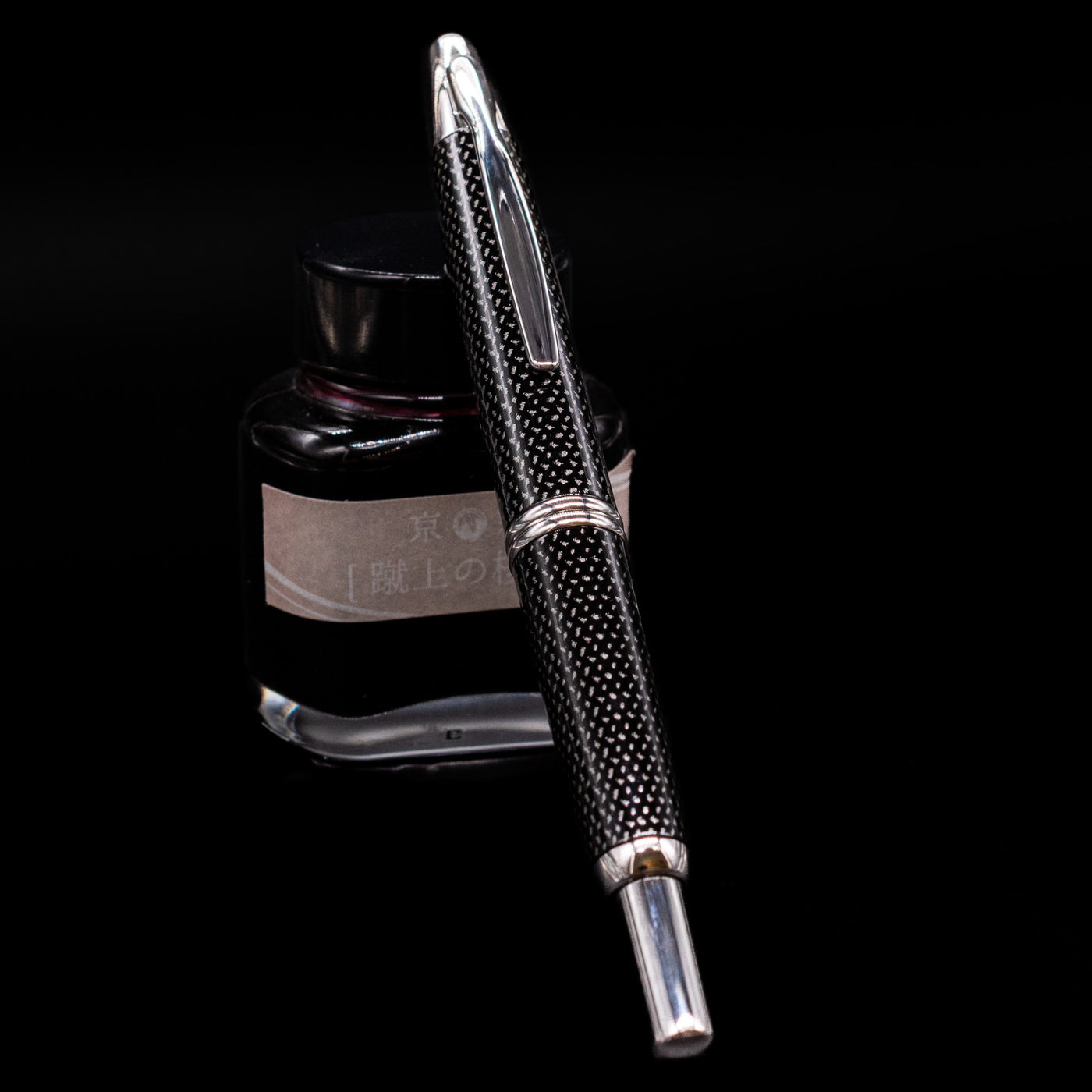 Pilot Vanishing Point Fountain Pen - Black Carbonesque capped, leaning against an ink bottle.