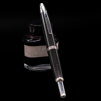 Pilot Vanishing Point Fountain Pen - Black Carbonesque capped, leaning against an ink bottle.