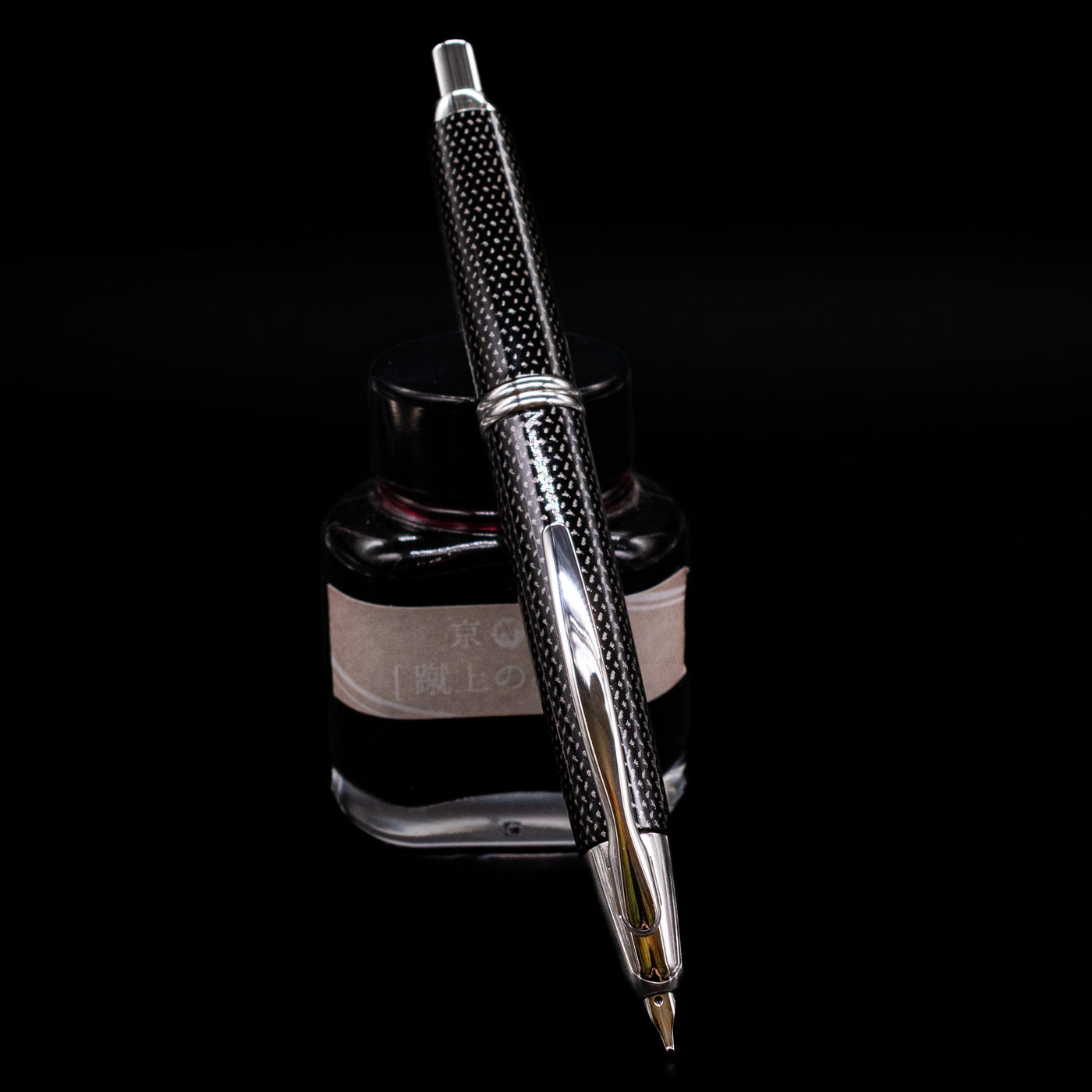 Pilot Vanishing Point Fountain Pen - Black Carbonesque uncapped, leaning against an ink bottle.