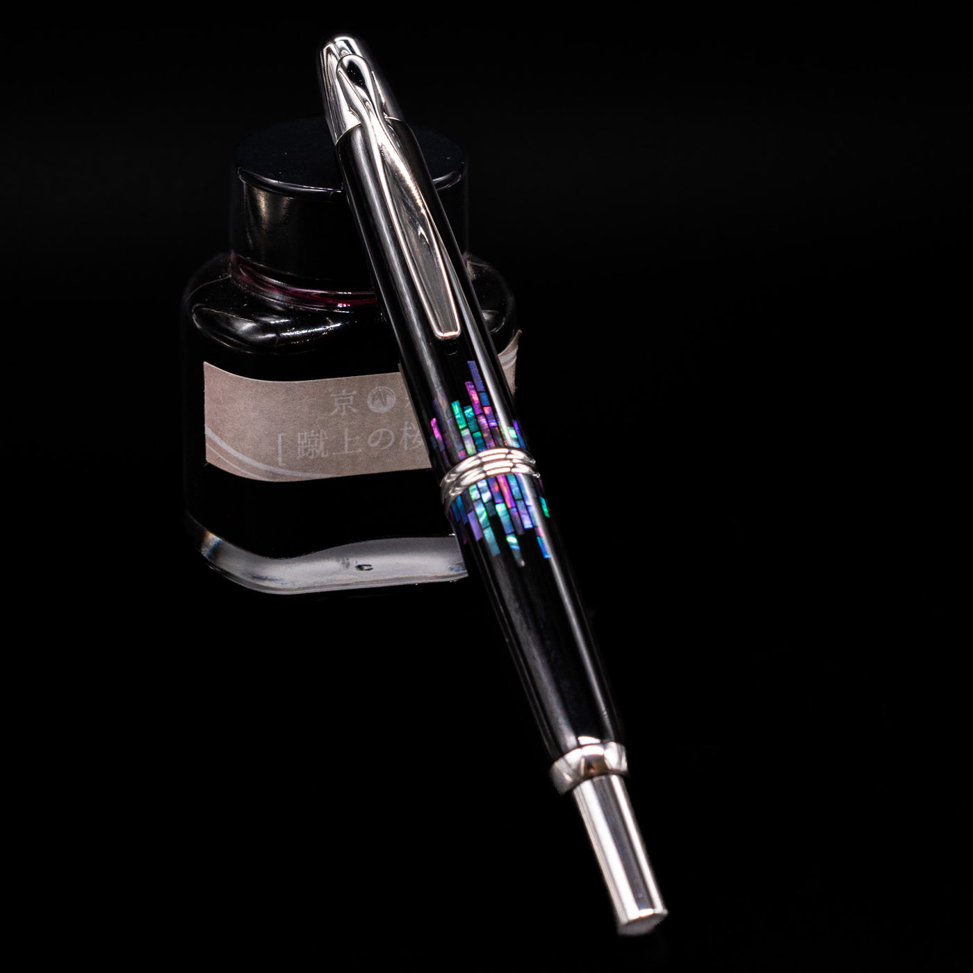 Pilot Vanishing Point Fountain Pen - Raden Stripe capped, leaning on an ink bottle.