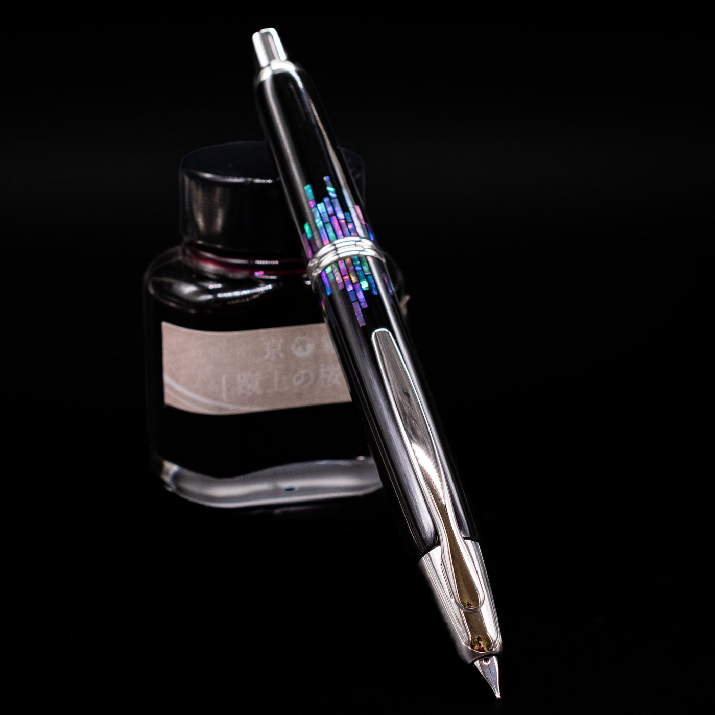 Pilot Vanishing Point Fountain Pen - Raden Stripe uncapped, leaning against an ink bottle, showcasing its nib.