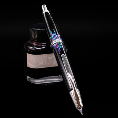 Pilot Vanishing Point Fountain Pen - Raden Stripe uncapped, leaning against an ink bottle, showcasing its nib.
