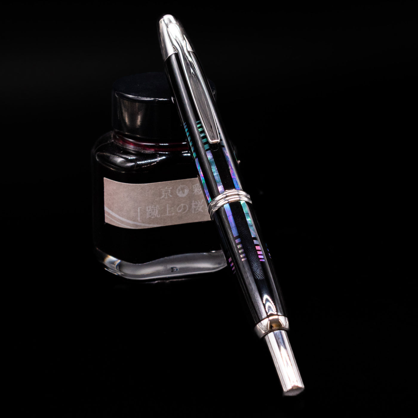 Pilot Vanishing Point Fountain Pen - Raden Water Surface capped, leaning against an ink bottle.