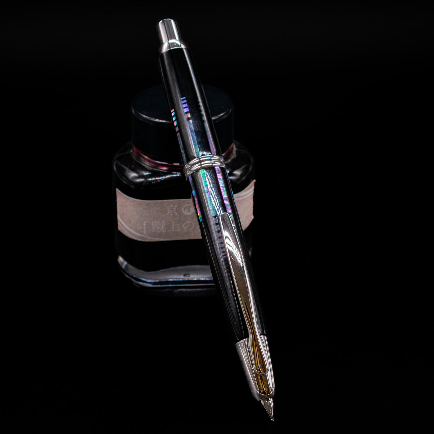 Pilot Vanishing Point Fountain Pen - Raden Water Surface uncapped, leaning on an ink bottle showcasing its nib.