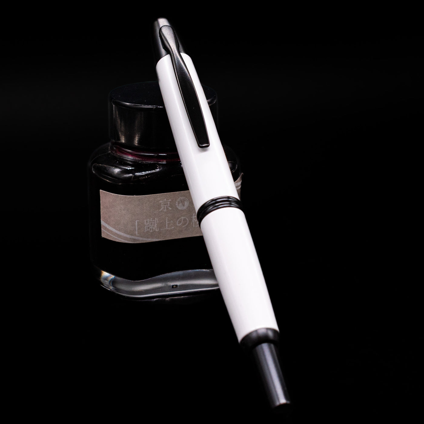 Pilot Vanishing Point Fountain Pen - White & Black capped, leaning against the ink bottle.