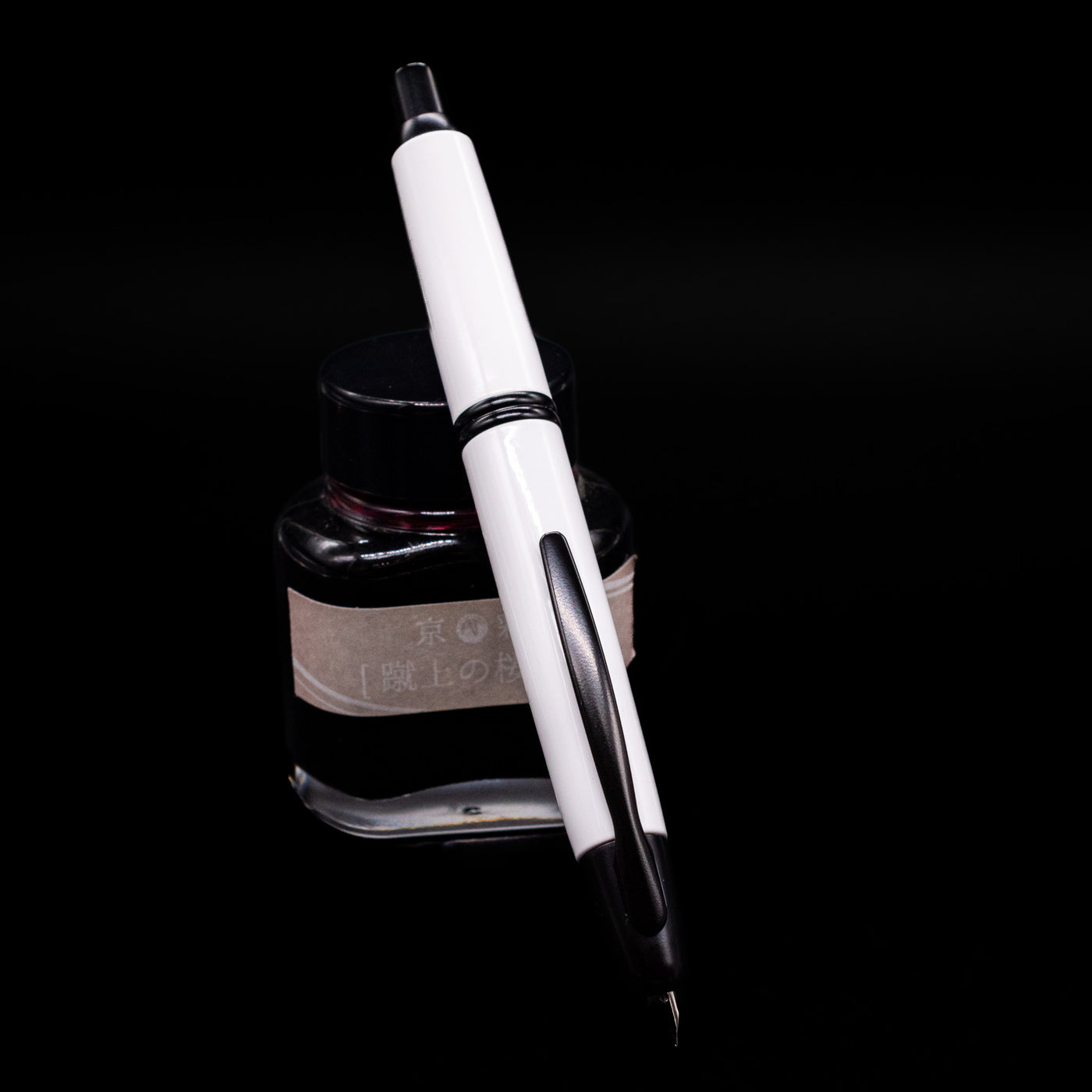 Pilot Vanishing Point Fountain Pen - White & Black leaning against an ink bottle, activated.