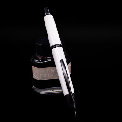 Pilot Vanishing Point Fountain Pen - White & Black leaning against an ink bottle, activated.