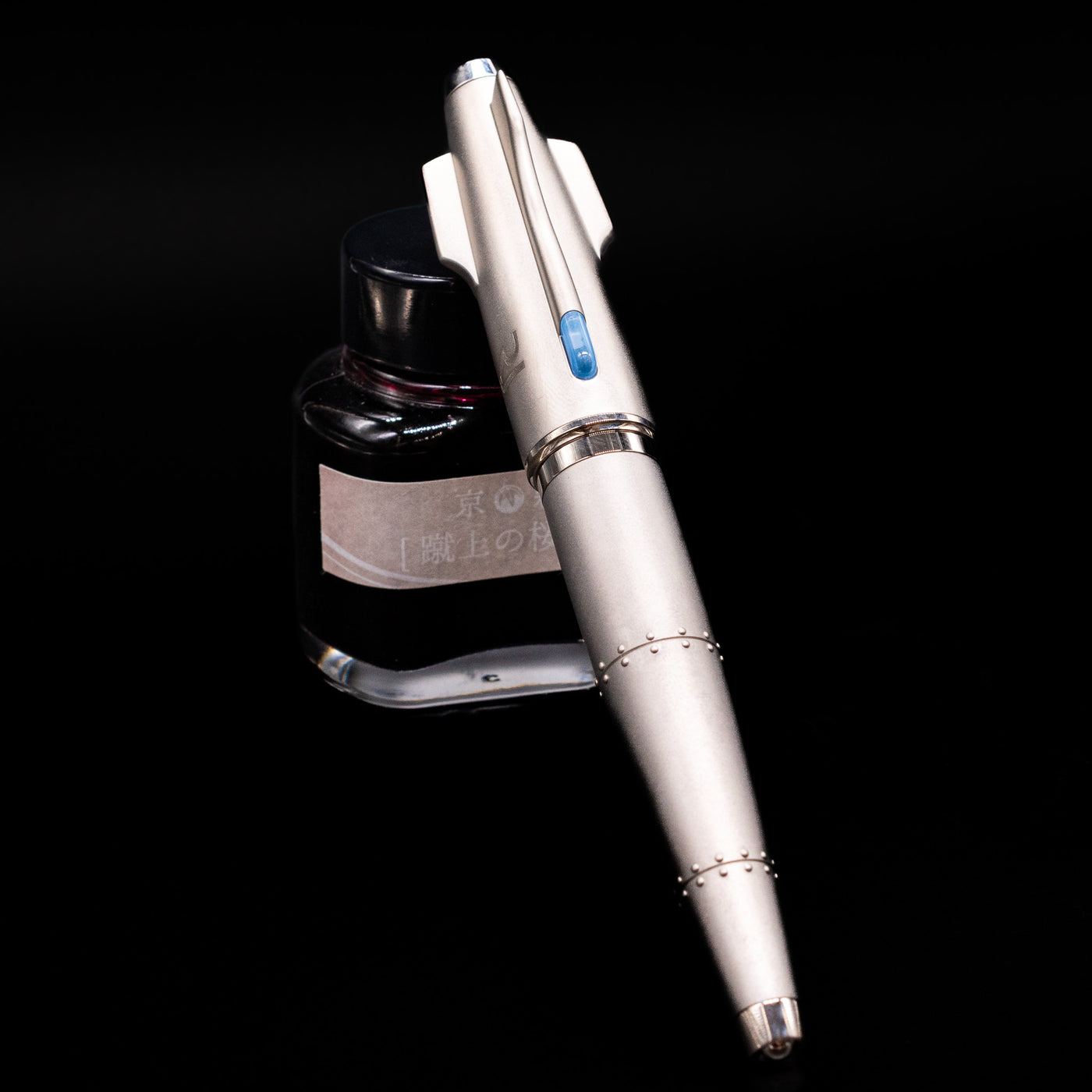 Romain Jerome Moon Fighter Rollerball Pen - Heavy Metal capped, leaning against an ink bottle. 