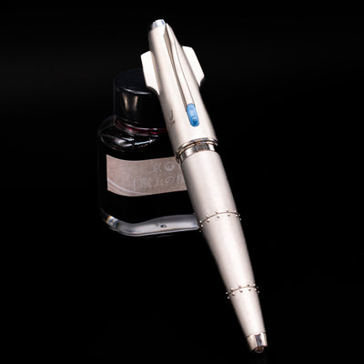 Romain Jerome Moon Fighter Rollerball Pen - Heavy Metal capped, leaning against an ink bottle. 