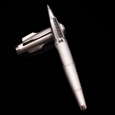 Romain Jerome Moon Fighter Rollerball Pen - Heavy Metal laying on top of its cap in a crossed position showing full view of the entire uncapped pen.