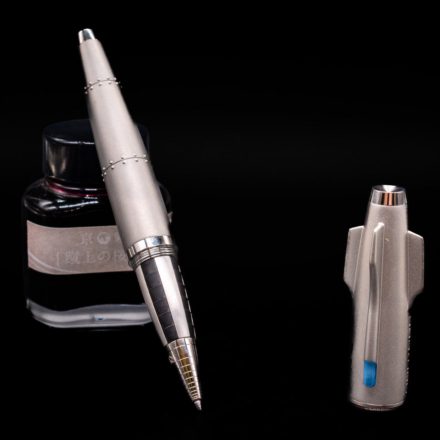 Romain Jerome Moon Fighter Rollerball Pen - Heavy Metal leaning on an ink bottle uncapped showcasing the detailing on the tip.