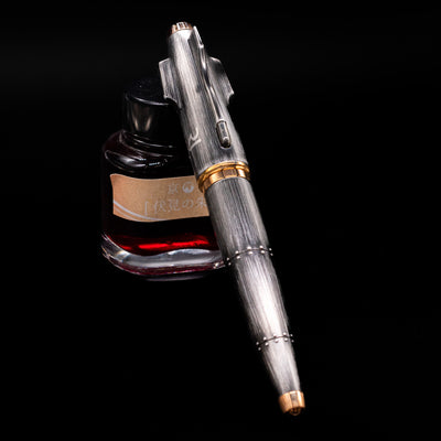 Romain Jerome Moon Fighter Rollerball Pen - Vintage Finish capped, leaning against an ink bottle. 