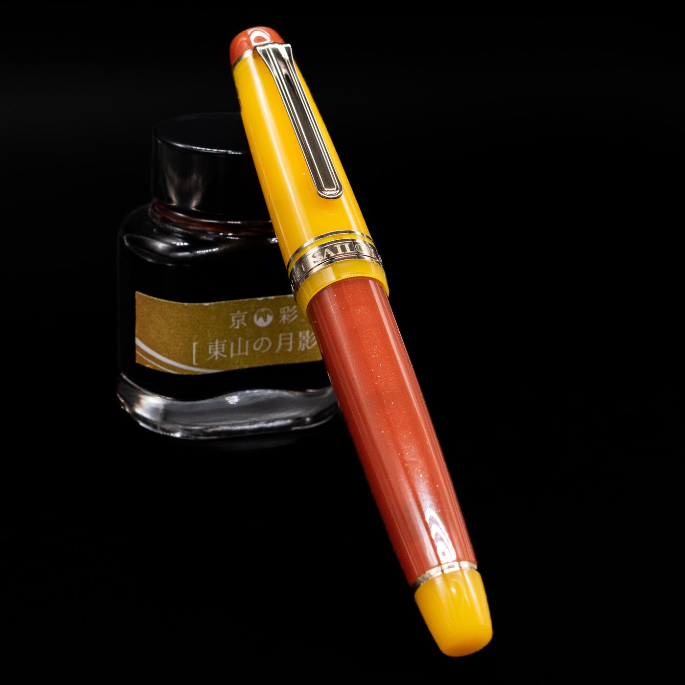Sailor Professional Gear King of Pens Fountain Pen - Moonlight Over the Ocean capped, leaning against an ink bottle.
