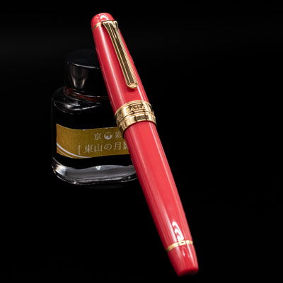 Sailor Professional Gear King of Pens Fountain Pen - Pillow Book Autumn Sky capped, leaning against an ink bottle. 