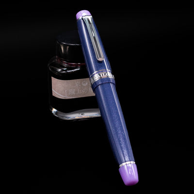 Sailor Professional Gear King of Pens Fountain Pen - Storm over the Ocean capped, leaning against an ink bottle. 