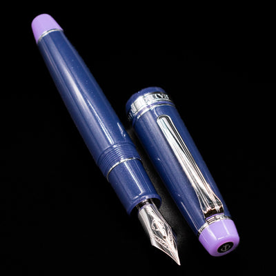 A full view of the Sailor Professional Gear King of Pens Fountain Pen - Storm over the Ocean uncapped, with its cap laying next to the pen. 