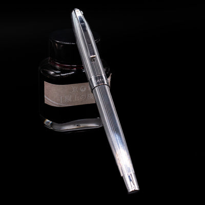 Sheaffer Sagaris Rollerball Pen - Chrome capped, leaning against an ink bottle. 