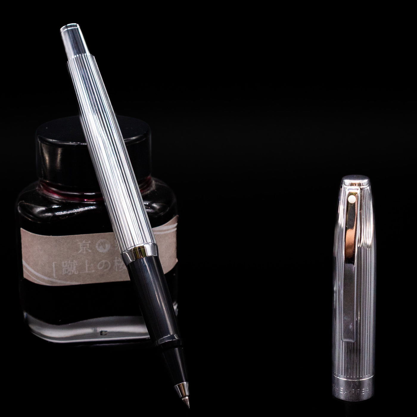 Sheaffer Sagaris Rollerball Pen - Chrome leaning on an ink bottle uncapped.