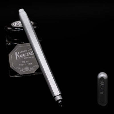 Stilform ARC Gel Pen – Comet Grey Aluminum leaning on an ink bottle uncapped showcasing the detailing on the nib.