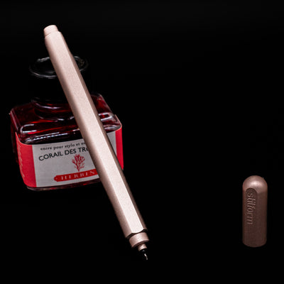 Stilform ARC Gel Pen – Rose Moon Aluminium leaning on an ink bottle uncapped showcasing the tip.