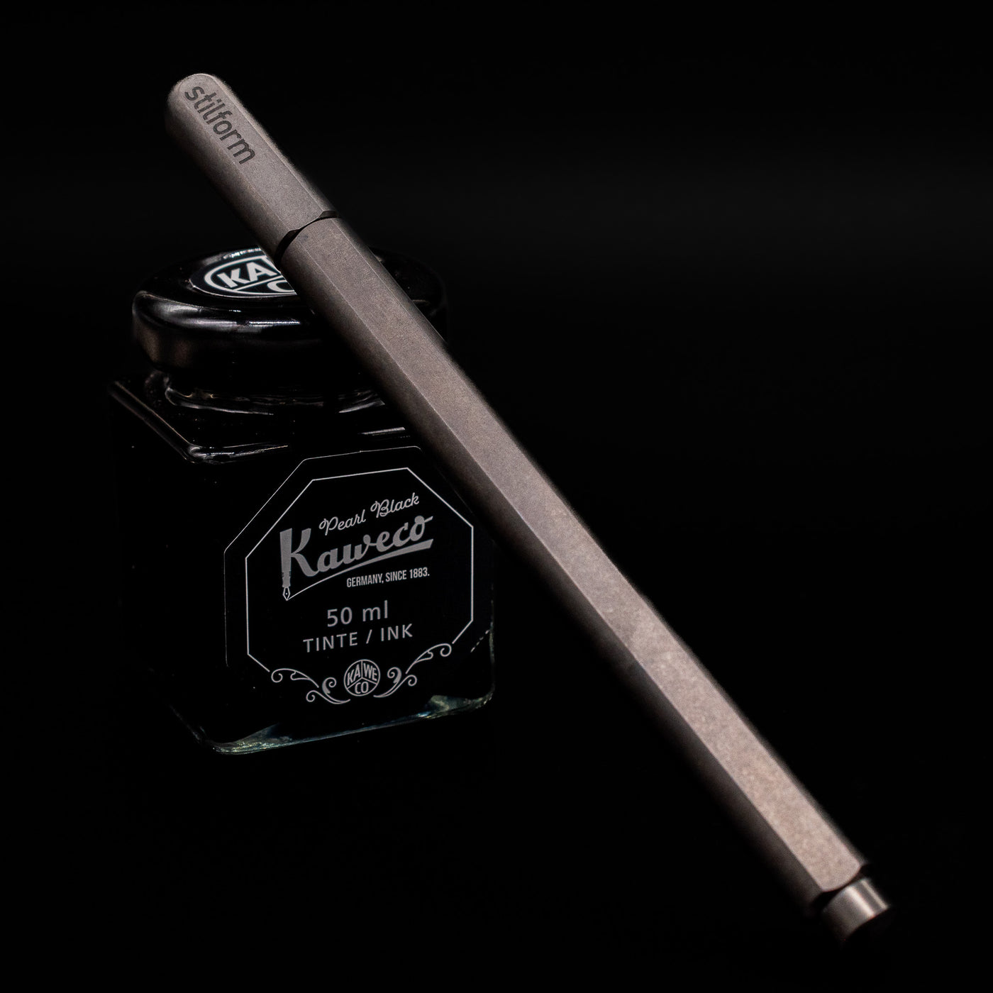 Stilform ARC Gel Pen – Titanium DLC capped, leaning against an ink bottle.