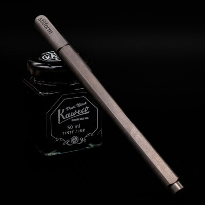 Stilform ARC Gel Pen – Titanium DLC capped, leaning against an ink bottle.