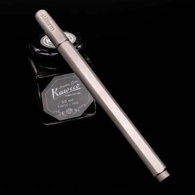 Stilform ARC Gel Pen – Titanium Matte capped, leaning against an ink bottle. 