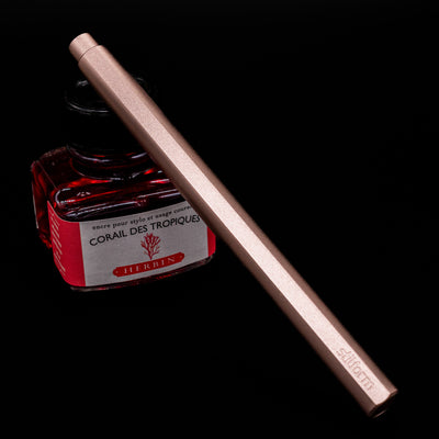 Stilform FLOW Rollerball Pen – Rose Moon Aluminium leaning on an ink bottle capped.